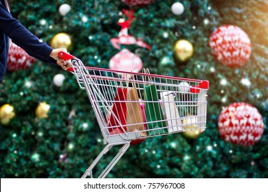 Christmas shopping - woman shopper with bags in shopping cart on holidays ornament and christmas tree on street background