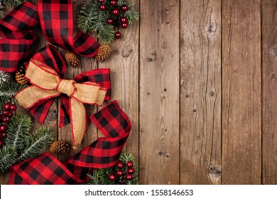 Christmas side border with red and black checked buffalo plaid ribbon, burlap and tree branches. Overhead view on a rustic wood background.