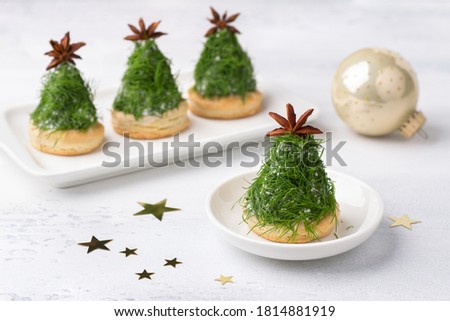 Christmas snack in the form of trees. Delicious cream cheese canapes with nuts, garlic and chopped dill on homemade puff cookies, decorated with a anise star. on light gray background with copy space