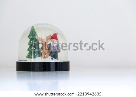 Christmas snow globe featuring Santa Claus, his reindeer and a Christmas tree, on white snowy background, festive ornament decoration, copy space on the right