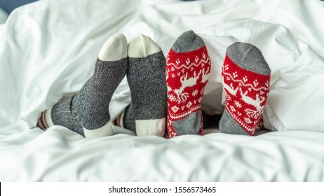 Christmas socks of family couple feet relaxing on bed having good sleep time together, enjoying resting at home in bedroom for winter holiday Xmas and New Year celebration - Powered by Shutterstock