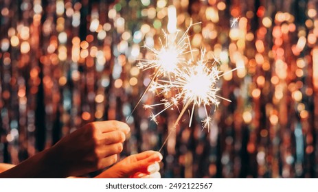 Christmas sparklers. Winter holidays. Festive mood. New year party. Female hands holding burning bengal fireworks on defocused glow bokeh lights tinsel decor background. - Powered by Shutterstock