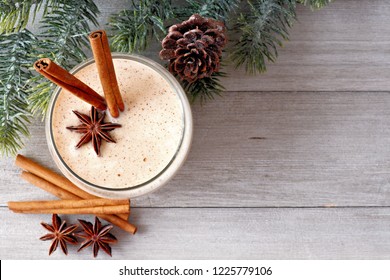 Christmas spiced eggnog in a glass. Top view, with corner border of tree branches on a rustic gray wood background. - Powered by Shutterstock