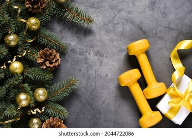 Christmas Sport Equipment: Yellow Dumbbells And Fir Branches, Presents, Christmas Decoration On A Gray Concrete Background. Fitness, Sport Or Healthy Lifestyle Concept. New Year. Christmas. Copy Space