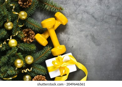 Christmas Sport Equipment: Yellow Dumbbells And Fir Branches, Presents, Christmas Decoration On A Gray Concrete Background. Fitness, Sport Or Healthy Lifestyle Concept. New Year. Christmas. Copy Space