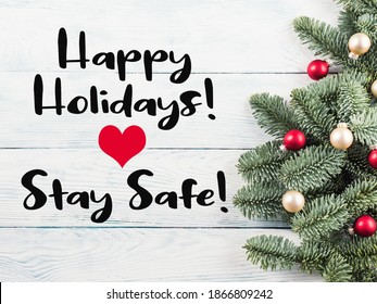 Christmas Spruce Branches With Red Golden Decor On Wooden Table. Greeting Card In Times Of Covid Pandemic With Text Happy Holidays, Stay Safe