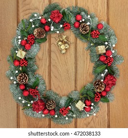 Christmas Spruce Fir Wreath Decoration With Red And Gold Bauble And Gift Box Decorations With Dangling Bells, Holly, Mistletoe And Pine Cones On Oak Front Door Background.