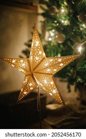 Christmas star on background of christmas tree in lights in evening room. Big paper star garland glowing in festive decorated scandinavian room. Atmospheric christmas eve. Happy holidays