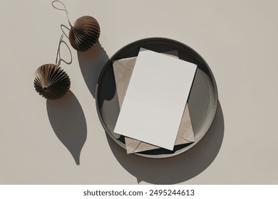 Christmas stationery mockup, ceramic plate. Blank greeting card, invitation template. Craft envelope, brown folded origami Christmas ornaments, balls in sunlight, beige table background. Flat lay, top - Powered by Shutterstock