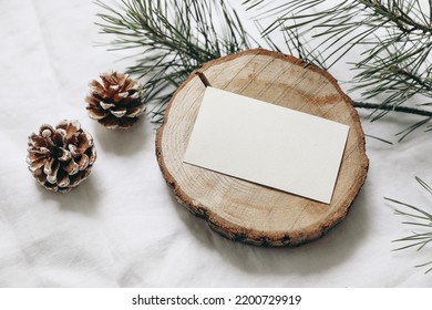 Christmas Stationery Still Life. Blank Business Card, Invitation Mockup On Cut Wooden Round Board. Pine Cones And Green Christmas Tree Branches On White Linen Cloth Background. Top View, No People.