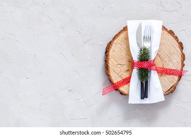 Christmas table place setting. Christmas serving cutlery with napkin, plate and logs cut on a concrete background. Christmas and New Year holidays background