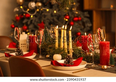 Christmas table setting with burning candles in room at night, closeup