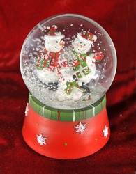 Christmas Themed Snow Globe Decoration Ornament With Snowman And Snow Against Crimson Red Velvet Background. Winter Festive Feliz Navidad Holiday Celebration