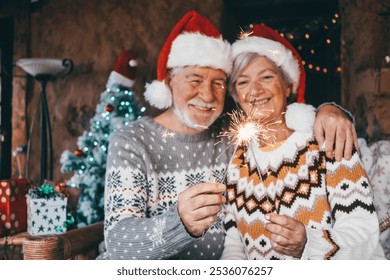 Christmas time. Blurred smiling elderly couple in Santa hats hugging at home lit by sparkles. Christmas tree, gifts and decorations in the background - Powered by Shutterstock