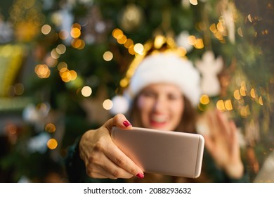 Christmas Time. Closeup On Smiling Woman With Santa Hat In Green Dress Having Web Cam Meeting On A Smartphone Near Christmas Tree In The House.