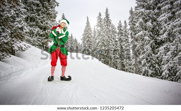 Christmas time and green young elf on winter road with\
snow 