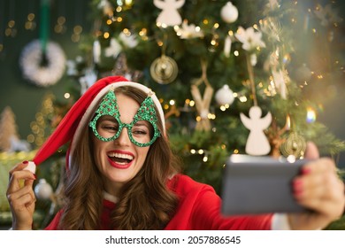 Christmas time. happy elegant 40 years old housewife with Santa hat answering incoming video call on a smartphone near Christmas tree in the modern house. - Powered by Shutterstock