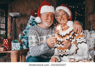 Christmas time. Portrait of blurred smiling senior couple in Santa hat holding sparkler lights at home. Celebration Christmas and new year concept - Powered by Shutterstock