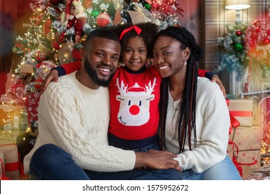 Christmas time. Portrait of cheerful black family of three celebrating winter holidays at home together, cuddling and smiling at camera