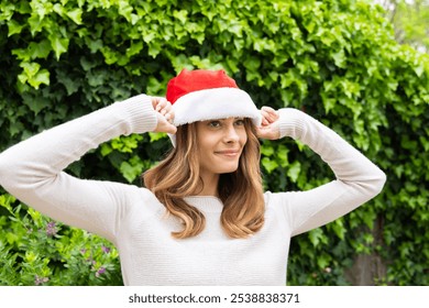 Christmas time, Smiling woman adjusting Santa hat outdoors, enjoying festive holiday season. Celebration, Christmas, winter, happiness, cheerful, joyful - Powered by Shutterstock