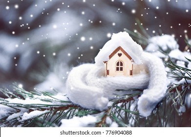 Christmas Toy house is wrapped in a warm scarf, it's snowing.on a natural natural background of a real fir in the snow, toned. Concept of winter, Christmas, new year,
 warm, cozy, loving, protecting t