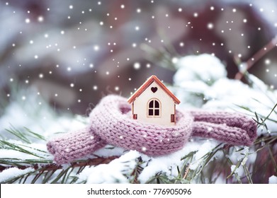 Christmas Toy House Is Wrapped In A Warm Scarf, It's Snowing.on A Natural Natural Background Of A Real Fir In The Snow, Toned. Concept Of Winter, Christmas, New Year,
 Warm, Cozy, Loving, Protecting 