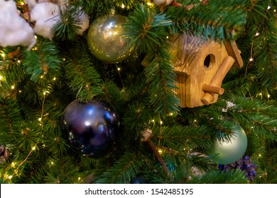 Christmas toys, balls of different colors, a birdhouse, a shining garland hanging on the branch of the Xmas tree. Close-up