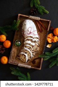 Christmas traditional fruit bread stollen lying down in a wooden tray on dark kitchen table, top down view on holliday treats