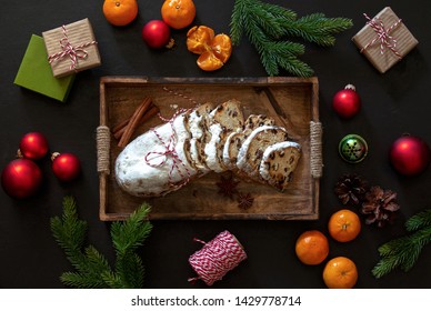 Christmas traditional fruit bread stollen lying down in a wooden tray on dark kitchen table, top down view on holliday treats, gift boxes and home Xmas decorations