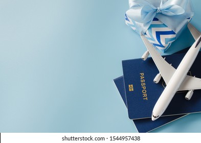 Christmas Travel Planning. Traveling As Gift. White Blank Model Of Passenger Plane, Passports And Gift Box On Blue Background. Top View Or Flat Lay. Copy Space.