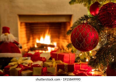 Christmas tree branch with red ornament balls, gift boxes with sparkle ribbons, bows and blur burning fireplace background. Xmas home celebration concept. Warm family moments. - Powered by Shutterstock