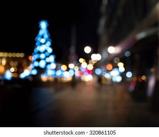 Christmas Tree In The City Square. Abstract Dark Blurry Urban Background. 