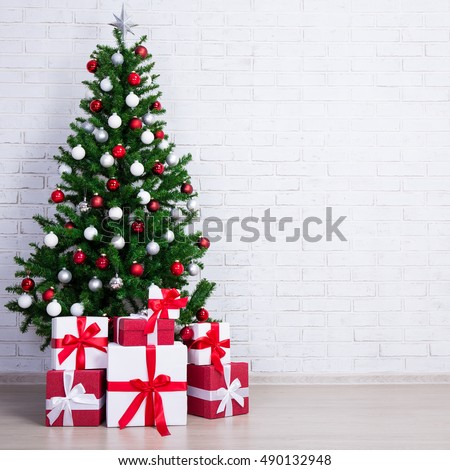 christmas tree with colorful balls and gift boxes over white brick wall