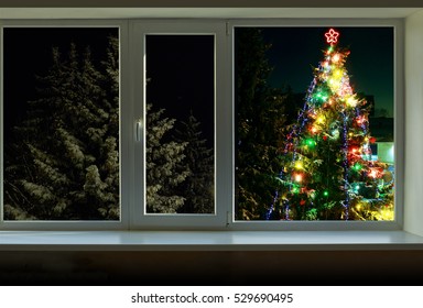 Christmas Tree Decorated With Bright Colored  Lights Is Outside The Window