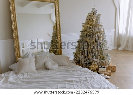 Christmas tree decorated with shiny threads in the apartment. Mattress and large mirror on the floor