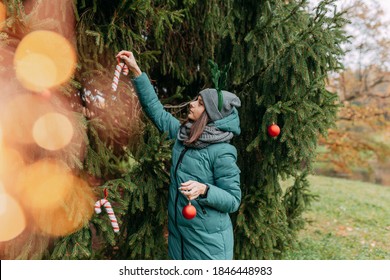 Christmas tree fir branches. Young woman decorating christmas tree outside. Decorative antlers on had. Christmas decorations, candy canes and balls.