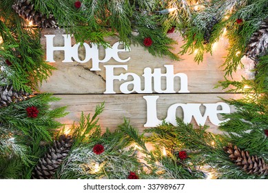 Christmas Tree Garland Border With Snow, Lights, And The Words Hope, Faith, Love On Antique Rustic Wooden Background