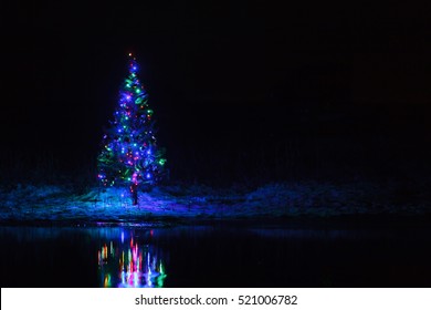 Christmas Tree With Garlands On A Background Of The Night Sky Reflected In The River.