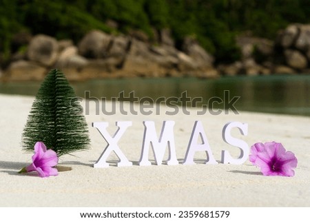 Christmas tree and inscription XMAS on a sandy beach with flowers