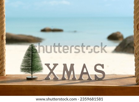 Christmas tree and inscription XMAS on a sandy beach with flowers