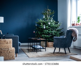 Christmas Tree In The Interior. Scandinavian Style, Minimalism. Dark Blue Wall, Grey Chair, Braided Baskets. White Paper Origami Toys.