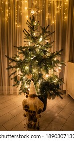 Christmas Tree With Lights And Santa Claus Figure In A Low-light Room, String Lights In The Background