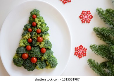 Christmas Tree Made Of Broccoli And Small Tomatoes On White Plate With Red Snowflakes And Fir Tree Branches On White Background. Healthy Organic Food. Festive Idea For Christmas And New Year Holidays 