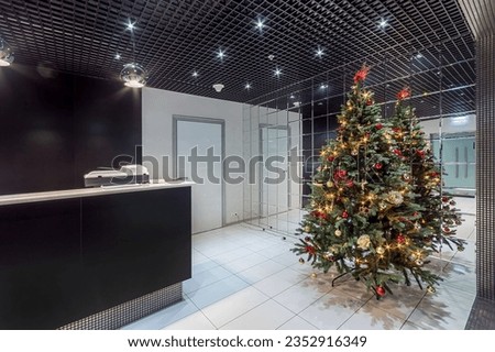 Christmas tree in a modern office lobby with an exclusive design. The room with a 
mirrored wall is decorated in black and white.