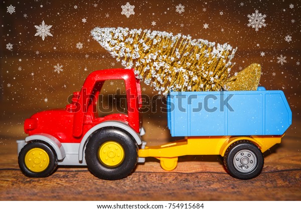 Christmas tree on toy tractor with trailer.\
Christmas holiday celebration concept with Snowflakes. New Year\
background.Toy truck carries Xmas\
tree.