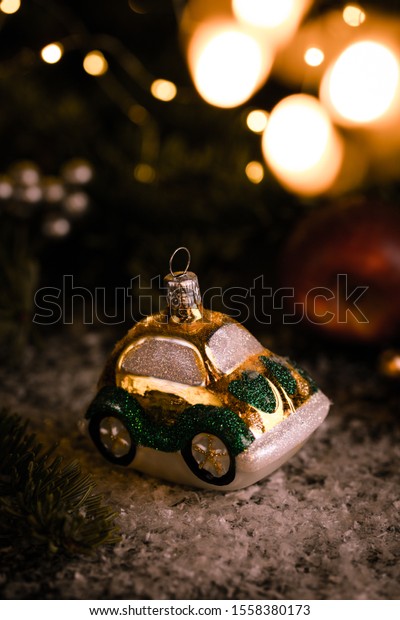 Christmas tree ornaments, tiny car on snowy table under
the fir tree and bokeh lights with white candle in the background.
Beautiful mysterious village decoration, greeting card, new year
celebration 