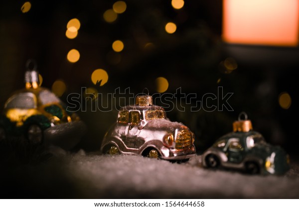 Christmas tree ornaments, tiny car on snowy table under\
the fir tree and bokeh lights with white candle in the background.\
Beautiful mysterious village decoration, greeting card, new year\
celebration 