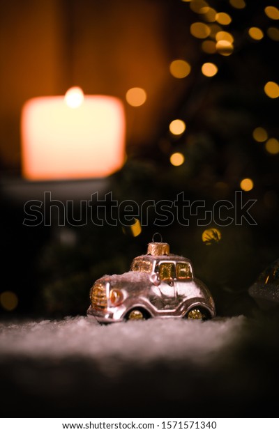 Christmas tree ornaments, tiny car on snowy table under\
the fir tree and bokeh lights with white candle in the background.\
Beautiful mysterious village decoration, greeting card, new year\
celebration 