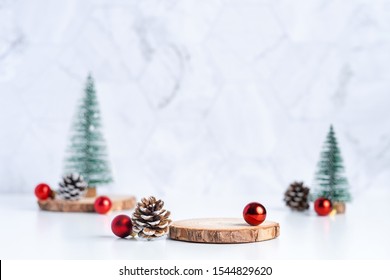 christmas tree with pine cone and decor xmas ball and empty wood log plate on white table and marble tile wall background.clean minimal simple style.holiday still life mockup to display design
