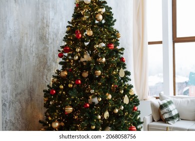 Christmas tree with red and gold balls and gold garland lights in a bright room. - Shutterstock ID 2068058756